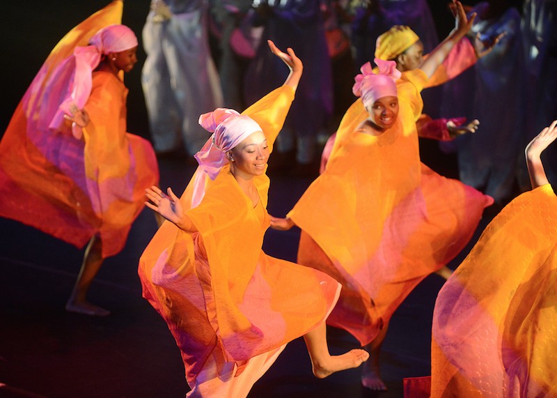 DanceAfrica Ensemble, Photography by Dino Perrucci- smiling women dancing covered in colorful large silks of orange and magenta with equally beautiful head scarves